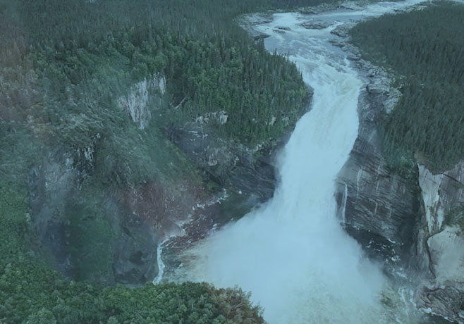 Aerial picture looking down at river and waterfall, surrounded by tees.